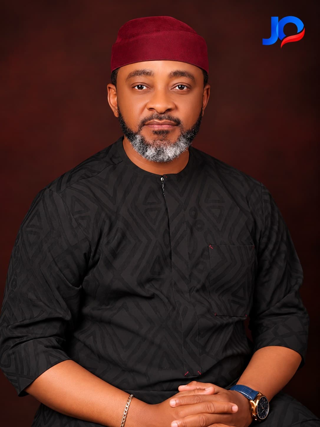 John Upan Odey Jnr in patterned traditional attire and a red cap, facing camera.