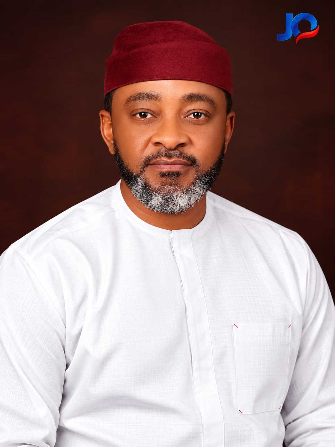 John Upan Odey Jnr in white traditional attire and a red cap, facing camera.