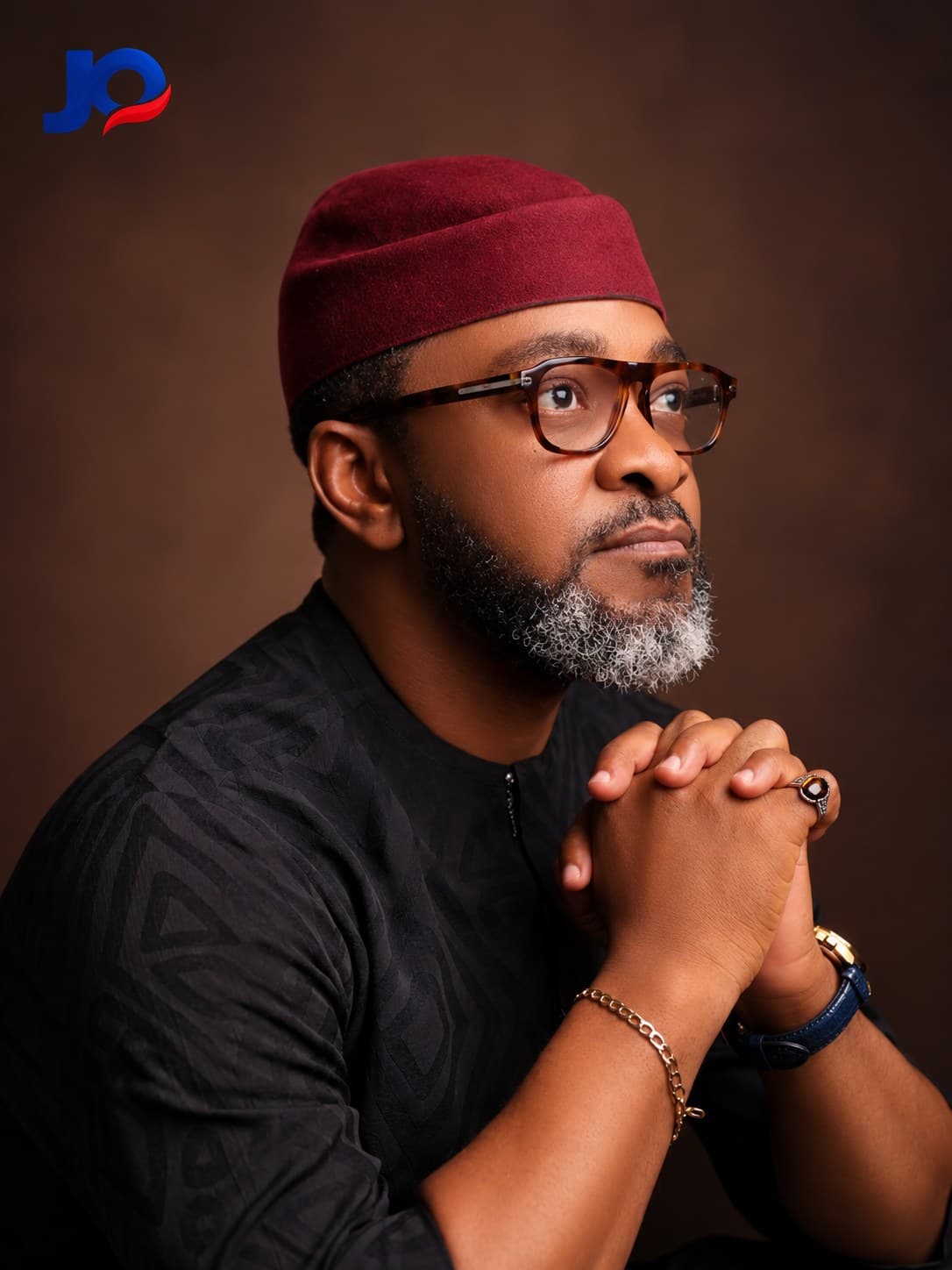 John Upan Odey Jnr in traditional attire and glasses, looking up.